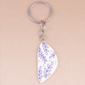 Detail of bohemian acrylic keychain with blue floral patterns on a white pendant - Geometric Leaves