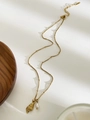 Dettaglio di collana dorata con ciondolo a conchiglia e perla barocca su bianco - Conchiglia Appuntita