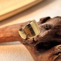 Gouden brede ring met horizontale gelaagde texturen op een houten ondergrond - Goud