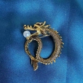 Nahaufnahme der goldenen Drachenbrosche mit Schuppentextur und Perle auf blauem Stoff - Goldener Drache Mit Weißer Perle