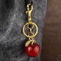 Red glitter apple keychain with gold metal clasp hanging on a grey textured bag - Red
