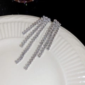 Nahaufnahme funkelnder langer Quastenohrringe mit Strass auf weißem Keramikteller - Silber (Silver Earring Post)