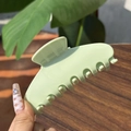 Medium matte sage green claw clip held by hand against a wooden and leaf background - Solid Milk Green - 7 Teeth Claw