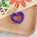 Dettaglio portachiavi a cuore in perle viola con moschettone dorato su vassoio di legno - Viola