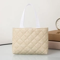 Close-up of beige quilted tote bag with white webbing handles on a white tabletop - Horizontal / Apricot