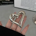 Polished silver heart-shaped metal hair claw clip held by hand for elegant hair styling - Heart Hollow / Silver