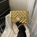 Detailed shot of a gold quilted crossbody bag with metal chain strap and rectangular clasp - Gold