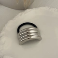 Close-up of elegant silver metallic layered hair tie on decorative ceramic plate - Textured Arc Style / Silver