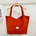 Close-up of orange canvas tote bag showing the front pocket and white Bonogeed brand tag - Vermilion Red