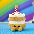Close-up of a cute plush cake toy with a smiley face and a red striped candle decoration. - 12cm (Rainbow Rope) / Brown