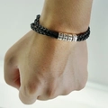 Gros plan d'un bracelet en cuir tressé noir avec perles métalliques gravées au poignet - Bracelet à Perles Argentées / 56cm et 1 Perle
