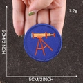 Round blue boy scout patch with orange telescope embroidery held by hand, 5cm diameter - Dark Blue Binoculars