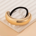 Macro view of golden curved metal hair tie with black elastic band on textured tray - Gold 1090575