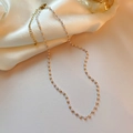 Detailed close-up of a gold-plated crown pearl necklace resting on elegant white silk fabric - Gold