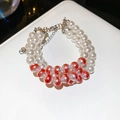 Macro view of double-layered pearl bracelet with silver-tone lobster clasp and red swirl beads - Multi-layer Beaded Bracelet / White-Red