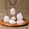 Irregular pink quartz stone pendant with black leather cord on a wooden display - Rose Quartz