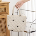 Detail of cream quilted tote bag featuring black embroidered bows and soft fabric texture - Beige Fabric with Embroidered Bow