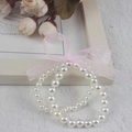 Close-up of white faux pearl bracelet with a pink mesh bow on a textured surface - Double Layer 6MM+8MM Cream Pearl With Pink Ribbon Bracelet