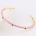 Detail of gold-plated bangle featuring pink enamel stripes and black circular accents - Pink