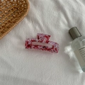 Detail of a pink marble acetate hair claw clip on white fabric with lifestyle props - Medium Square Claw / Blood Red
