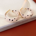 Macro shot of fabric-wrapped polka dot hoop earrings with gold metal accents - White