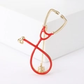 Close-up of a stethoscope brooch with red enamel details and gold-plated metal finish - Red
