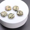 Five heart-shaped yellow spotted stone pendants with metal clasps on a white stand - Dalmatian Jasper