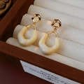 Detailed view of oval resin earrings with gold pleated texture on a velvet jewelry box - Off-white