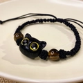 Macro shot of hand-woven black cord bracelet with a cute cat bead and tiger eye stones - Yellow Cat