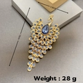 Dettaglio di una spilla a pavone dorata da 10cm con strass blu e dimensioni del prodotto - Base Oro Pietra Blu