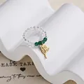 Elastic beaded ring with clear glass beads and green accents featuring a gold rose charm - Rose Flower Charm