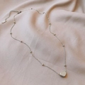 Gros plan du pendentif cœur et de la chaîne à billes sur fond en tissu rose - Style Perle Cœur X867 / Acier