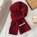 Gros plan d'une écharpe en tricot rouge vin avec étiquette blanche sur un lit douillet - Rouge Bonbon