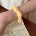 Artistic detail of a yellow irregular wavy acrylic cuff bracelet worn over an open book - Wave Irregular Bangle / Yellow