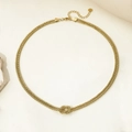 Detailed view of a gold knot pendant necklace with woven chain on a stone prop - Necklace / Gold