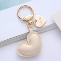 Detail of a beige leather heart keychain with gold 'Love' charm on white background - Off White