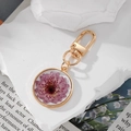 Detail of round gold keychain featuring real purple dried flowers in clear resin - Purple Cosmos