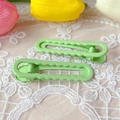 Detail of two green wavy hair clips on white lace with tulips in a soft natural setting - Green