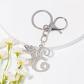 Makro-Detail des silbernen Strass-Buchstaben E und geflügelten Engel-Schlüsselanhängers - Stil E / Silber