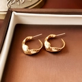 Primer plano detallado de pendientes de nudo dorado en un joyero marrón de lujo - Superficie curva geométrica irregular (1# Silver Earring Post-Dorado)