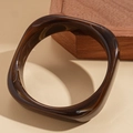 Detailansicht eines braunen Schildpatt-Resin-Armreifs auf einem Holz-Displayblock - Braun