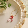 Détail d'un collier chaîne dorée avec pendentifs en émail rose et rouge sur un plat en céramique - Style-R