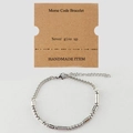 Detalle de pulsera plateada con código Morse, tarjeta Never Give Up y cierre de mosquetón - Never give up Plateado