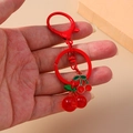 Kreativer roter Kirsch-Schlüsselanhänger mit Metallring und glänzenden Fruchthängern in der Hand - Kirsche