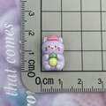 Macro view showing a tiny purple resin cartoon cat charm with a pineapple on a grid mat - Purple Pineapple Cat