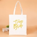 White canvas Team Bride tote bag with gold glitter text on a soft pink background - 26x33cm / Team Bride Gold Logo
