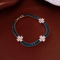 Macro detail of gold-plated bracelet with blue stones and white flower accents - Gold-Blue