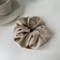 Detailed close-up of champagne silk scrunchie on a wooden stand with elegant pleats - Beige