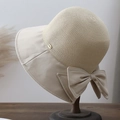 Detail of a straw sun hat featuring a beige fabric brim, large bow, and metal logo plate - Beige