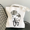 White canvas tote bag featuring a cute cartoon cat riding a bicycle on a black chair - Cat Riding Bicycle